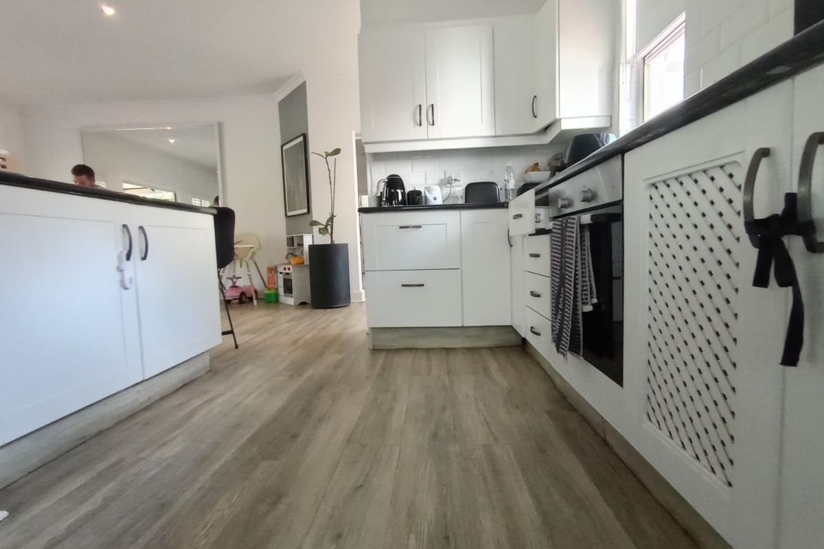 Modern kitchen featuring white shaker cabinetry, subway tile backsplash, dark countertops, and a central island, finished with durable wood-look laminate flooring.