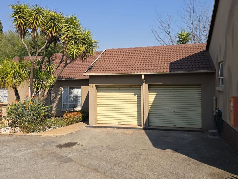 Front elevation of a townhouse featuring a double garage with roller doors, tiled roof, and paved driveway access.