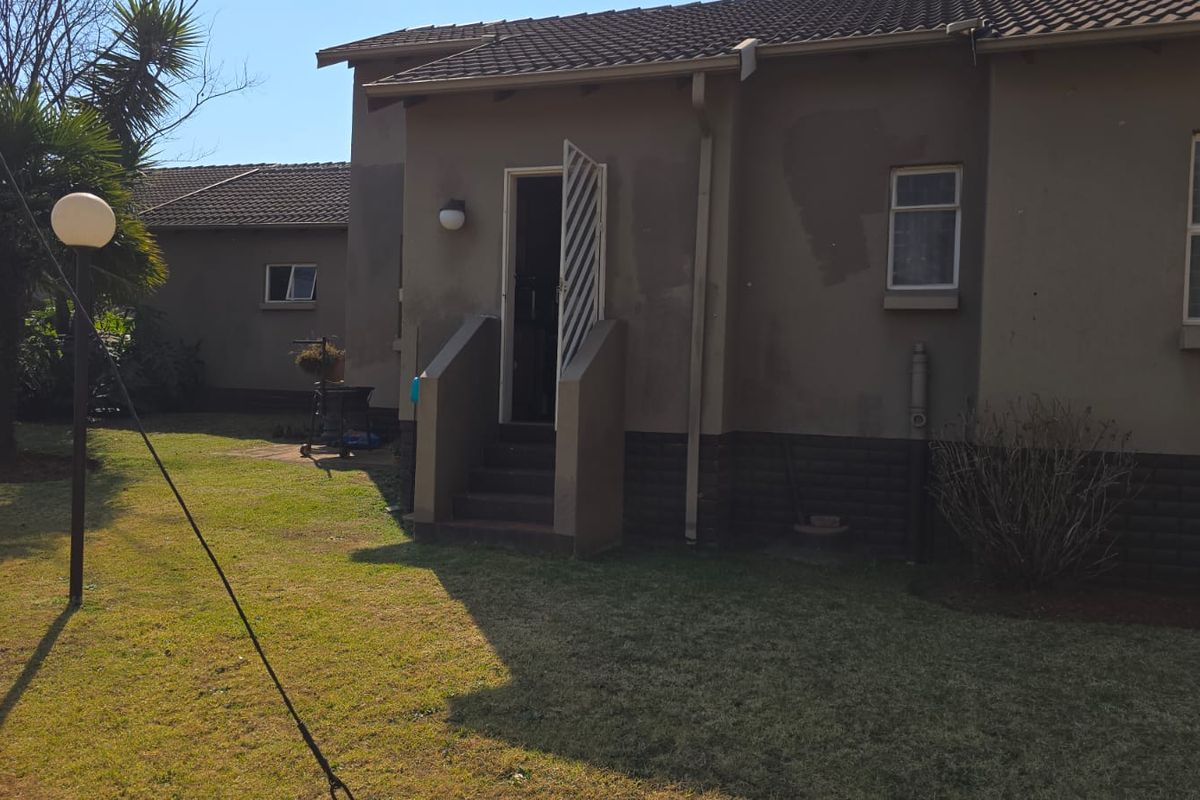 Rear view of the townhouse featuring a small garden area, concrete steps leading to the entrance, and a tiled roof structure.