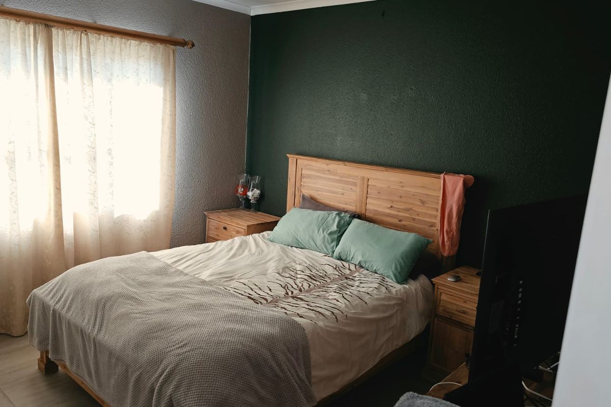 A bedroom featuring tiled flooring and a dark accent wall, providing a functional space with natural light from the window.