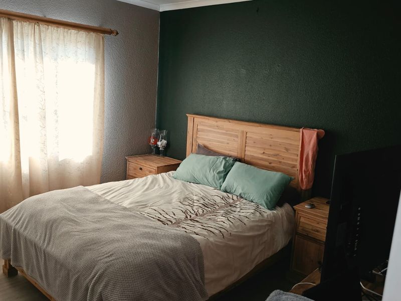 A bedroom featuring tiled flooring and a dark accent wall, providing a functional space with natural light from the window.