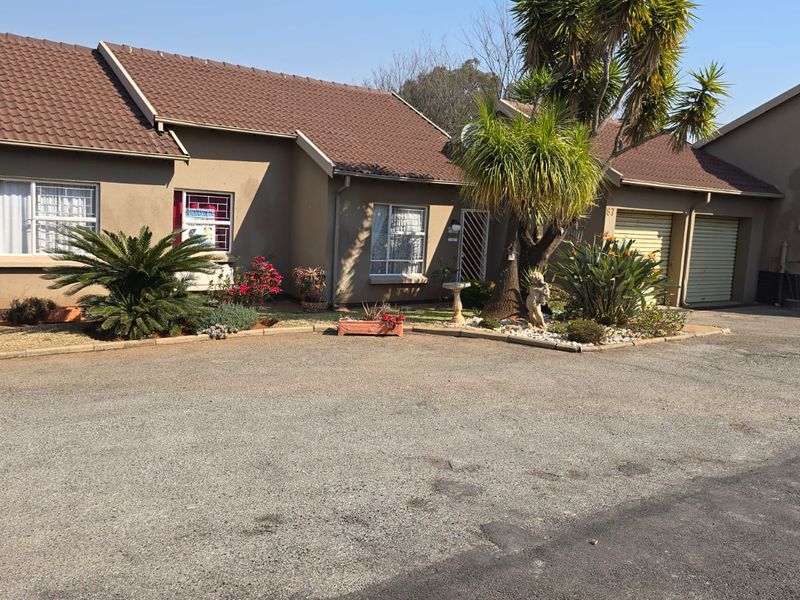 Front elevation of a townhouse featuring a tiled roof, double garage, and paved driveway with established garden beds.