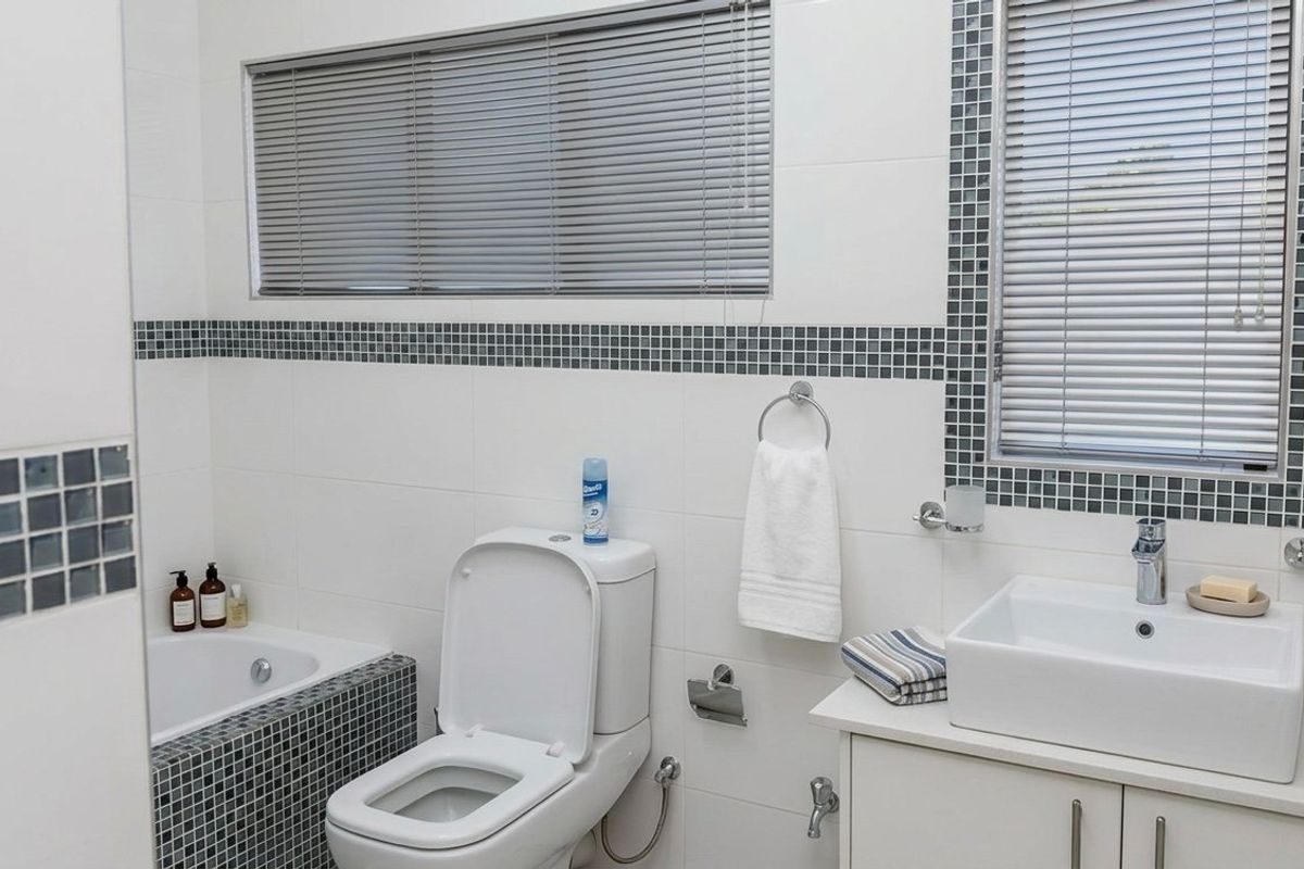 A clean, functional bathroom featuring a built-in bathtub, a modern vessel sink with vanity storage, and decorative mosaic tile accents.