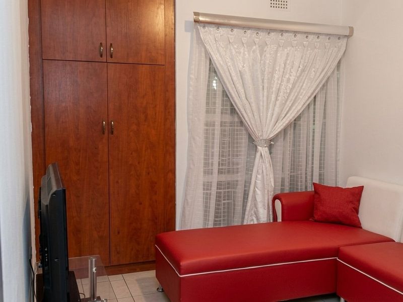 A bedroom featuring a built-in wooden wardrobe, tiled flooring, and a window with installed curtain rails.