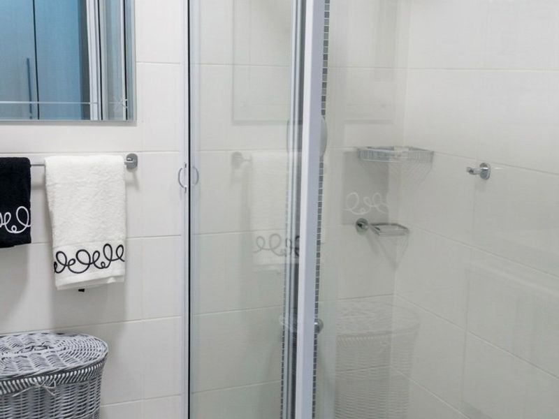 A clean, modern bathroom featuring a glass-enclosed shower with a rain shower head, white wall tiling, and a wall-mounted mirror.