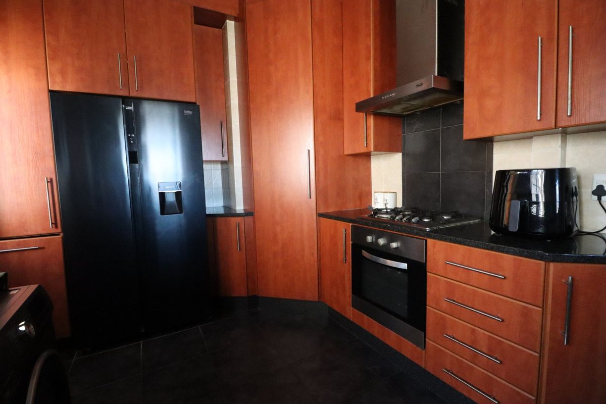 A functional kitchen featuring warm-toned wooden cabinetry, granite countertops, a gas hob, built-in oven, and dark tiled flooring.