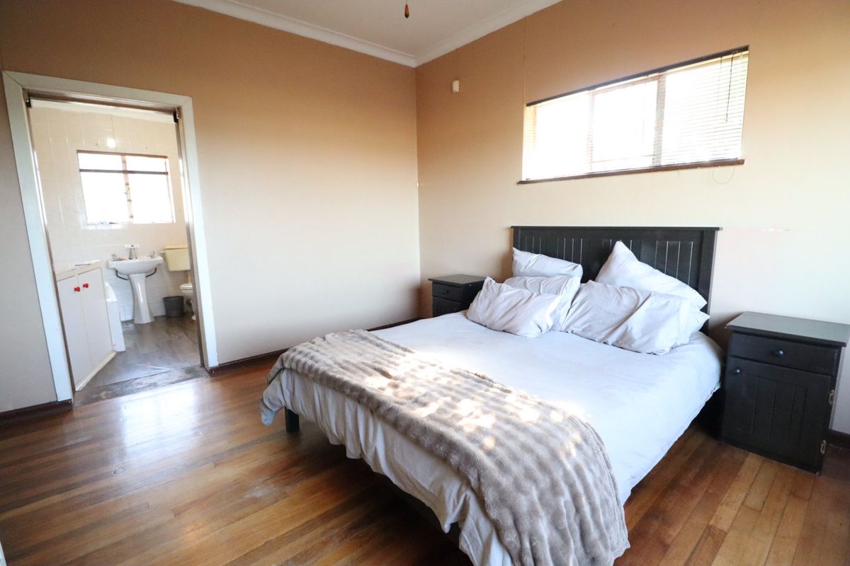Spacious bedroom featuring hardwood flooring and an attached en-suite bathroom with a pedestal sink and toilet.