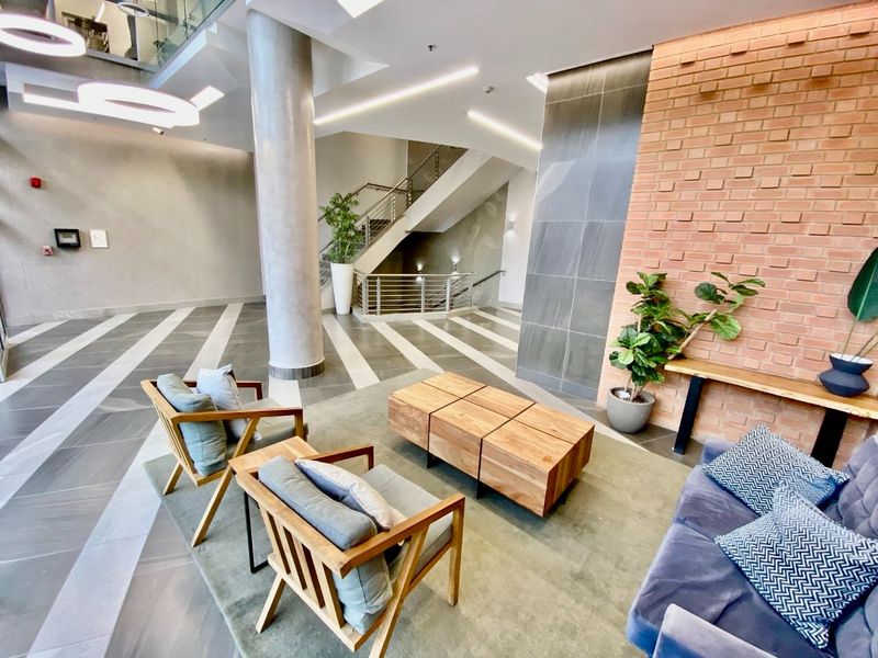 Modern commercial building lobby featuring an exposed brick wall, stone cladding, large format tiling, and a prominent staircase with metal balustrades.