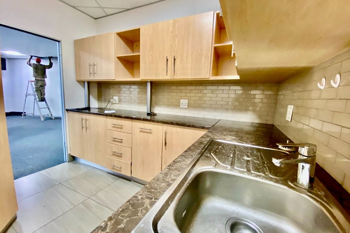 A functional kitchenette featuring light wood cabinetry, dark laminate countertops, a stainless steel sink, and a subway tile backsplash.