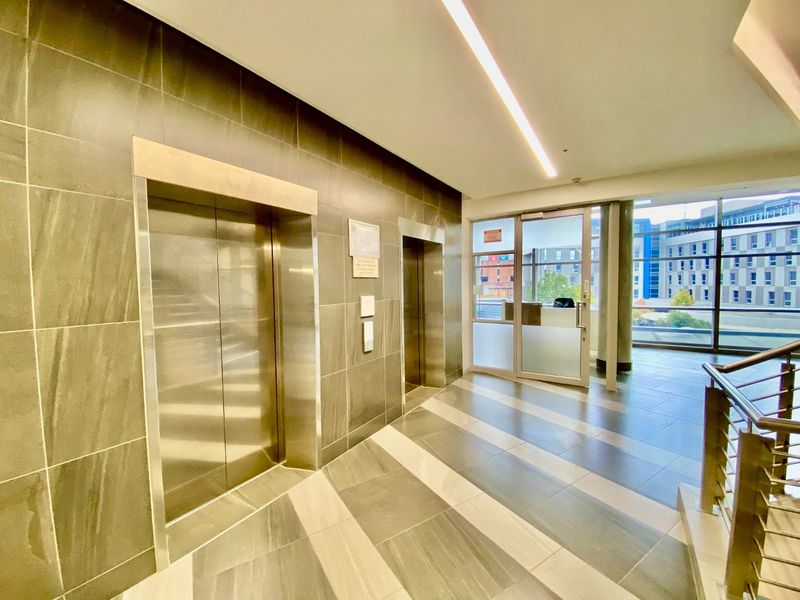 Modern commercial building lobby featuring tiled flooring, stainless steel elevator access, and glass entrance doors with natural light.