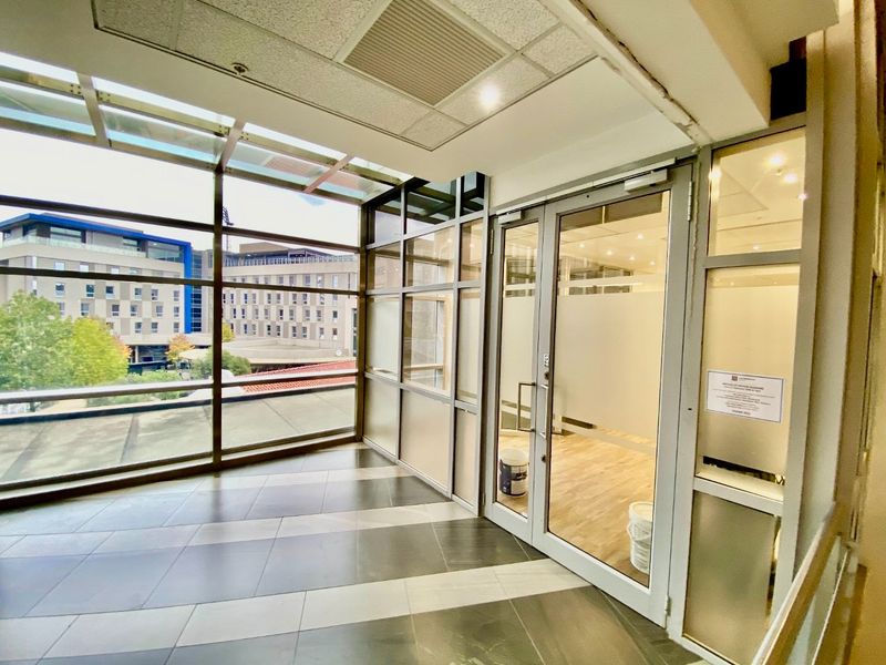 A bright commercial entrance lobby featuring floor-to-ceiling glass windows, tiled flooring, and a glass-paneled door leading into an office space.