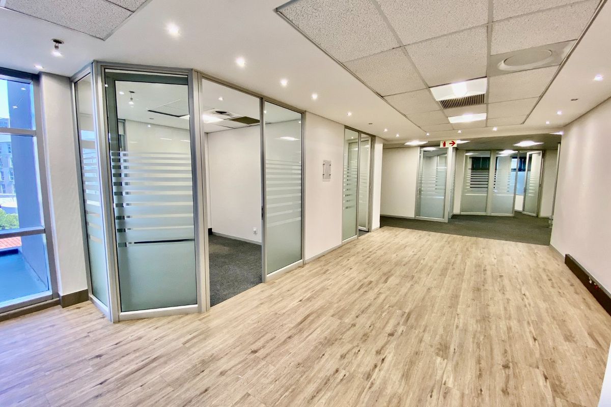 Modern commercial office space featuring glass-partitioned private offices, suspended ceilings with recessed lighting, and a combination of laminate and carpet flooring.