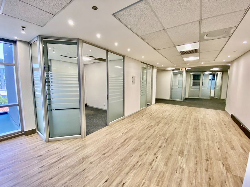 Modern commercial office space featuring glass-partitioned private offices, suspended ceilings with recessed lighting, and a combination of laminate and carpet flooring.