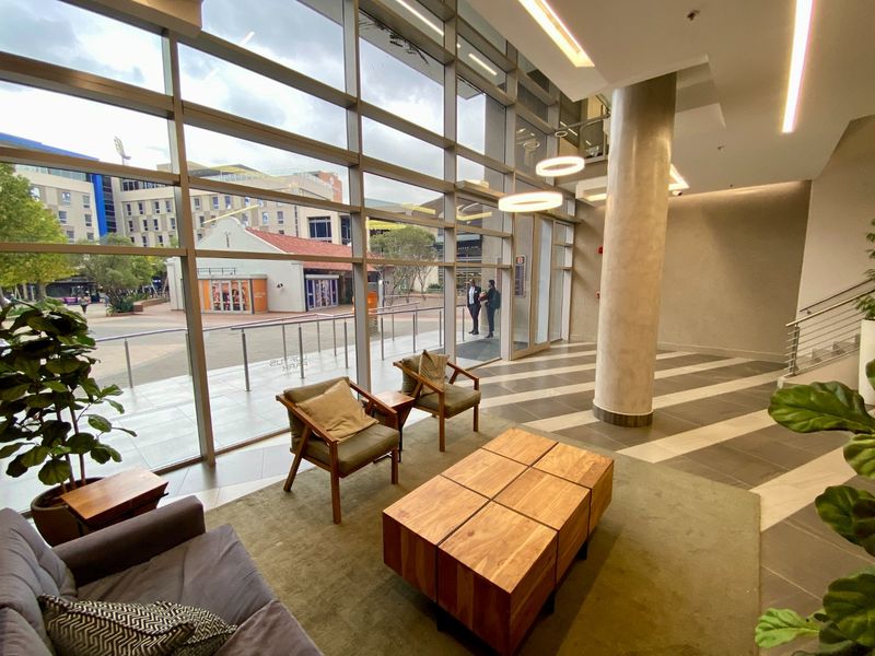 Modern commercial building entrance lobby featuring expansive floor-to-ceiling windows, high ceilings, recessed lighting, and a prominent structural column.