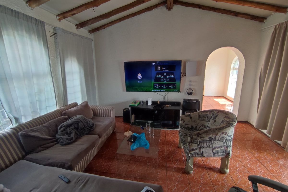 Living room featuring exposed timber ceiling beams, tiled flooring, and an arched doorway leading to an adjacent space.