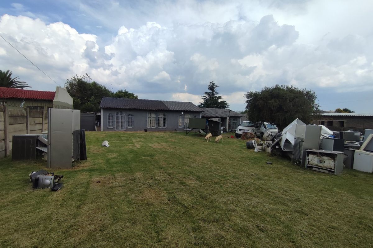 Rear view of the property featuring a large lawn area, tiled roof structure, and perimeter boundary walling.