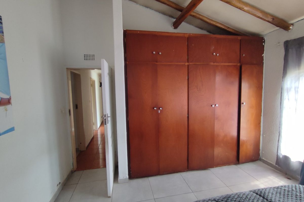 Bedroom featuring built-in wooden cabinetry, exposed timber ceiling beams, and tiled flooring, offering a functional space with potential for cosmetic updates.
