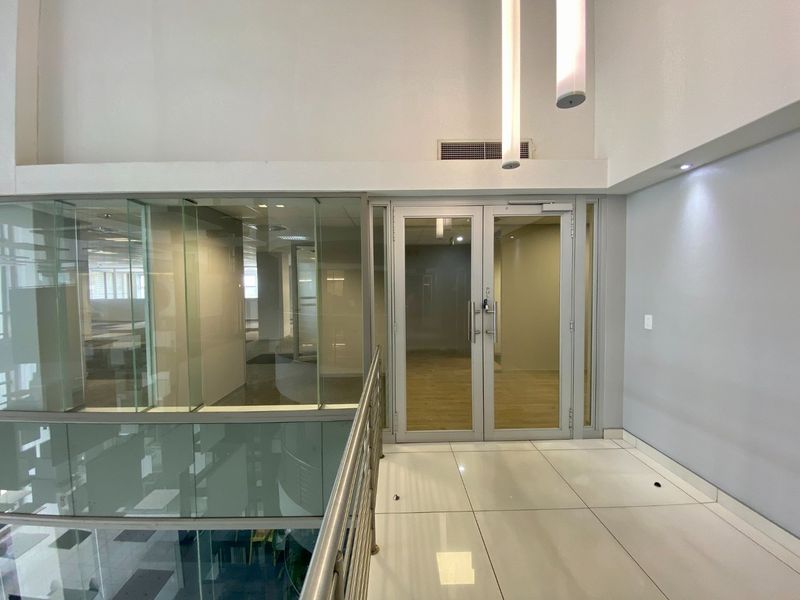 A bright, modern commercial hallway featuring glass partitions, double glass doors, and polished tile flooring with a stainless steel balustrade.