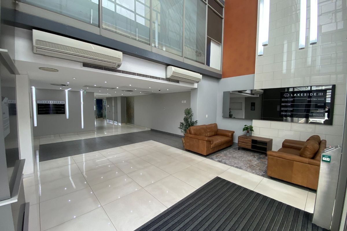 Spacious commercial building lobby featuring double-volume ceilings, large glass windows, tiled flooring, and integrated directory signage.