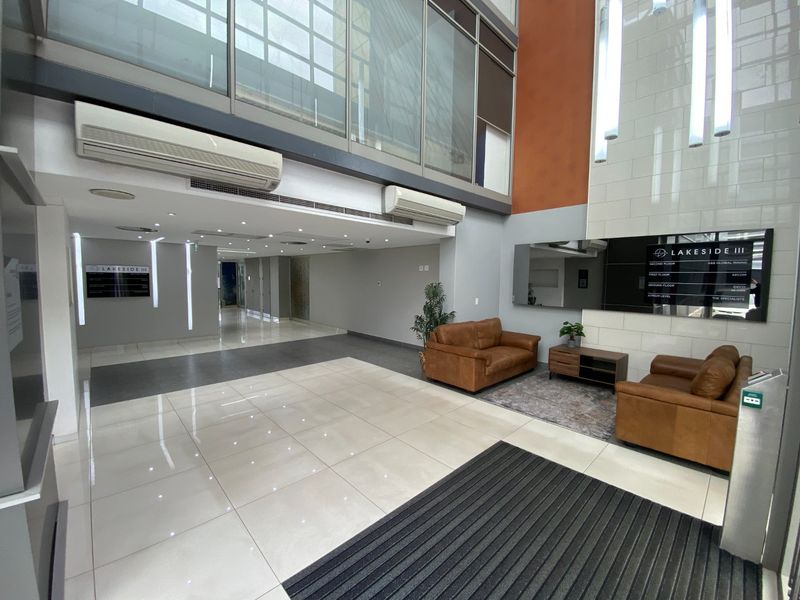 Spacious commercial building lobby featuring double-volume ceilings, large glass windows, tiled flooring, and integrated directory signage.