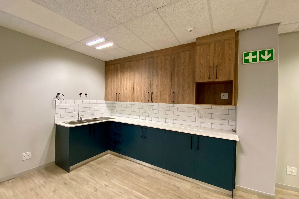 A modern, clean kitchenette featuring dark blue lower cabinets, wood-grain upper cabinets, white subway tile backsplash, and durable laminate countertops in a commercial office space.