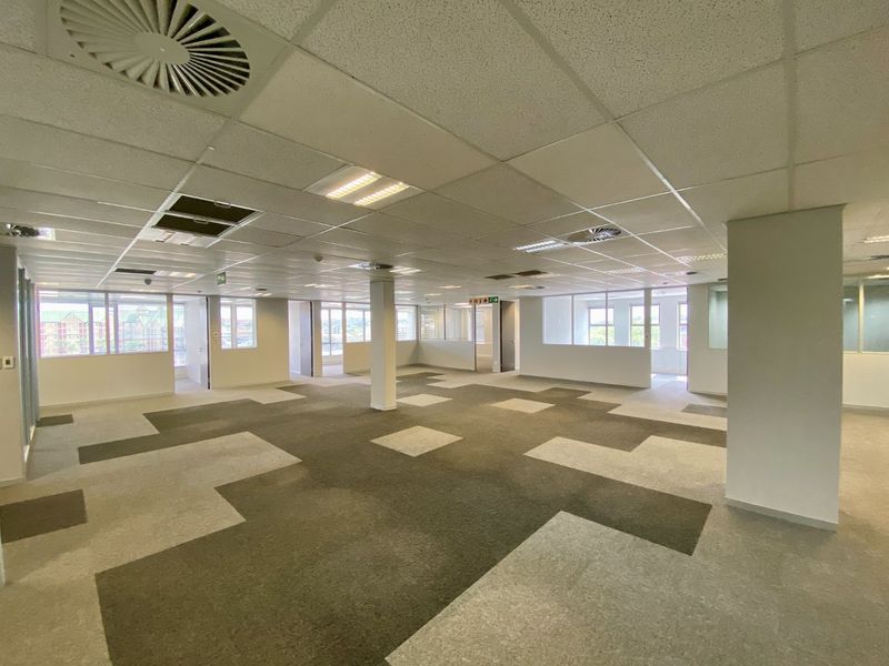 Open-plan commercial office space featuring suspended ceilings, recessed lighting, air conditioning, and modular carpet tiles with partitioned glass wall sections.