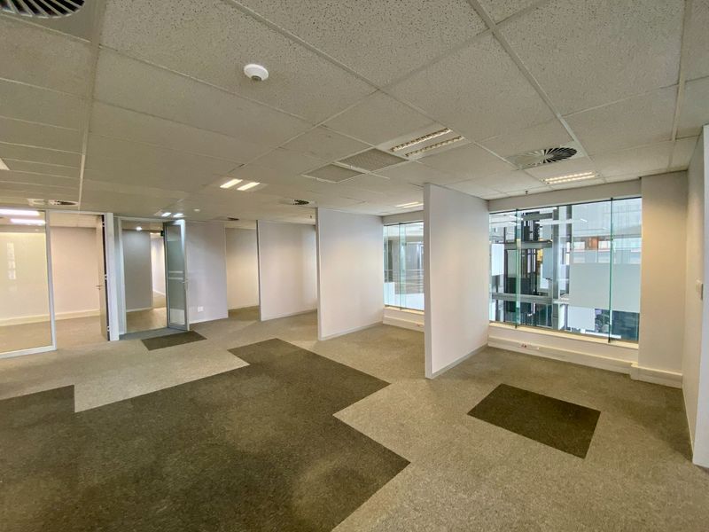 An open-plan commercial office space featuring glass partitions, suspended ceilings with recessed lighting, and modular carpet flooring.