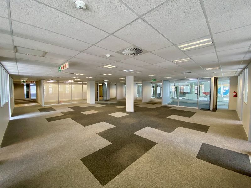 Spacious open-plan commercial office area featuring suspended ceilings, recessed lighting, carpet tiles, and glass-partitioned meeting rooms.
