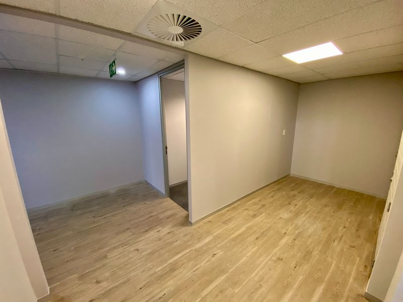 A clean, vacant commercial office space featuring modern laminate flooring, a suspended ceiling with recessed lighting, and integrated air conditioning.