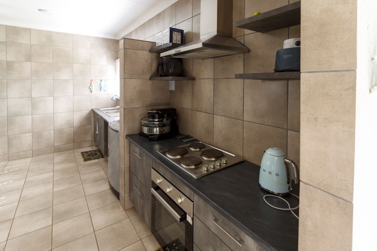 A functional kitchen area featuring built-in cabinetry, a stainless steel oven and hob, extractor fan, and tiled flooring throughout.