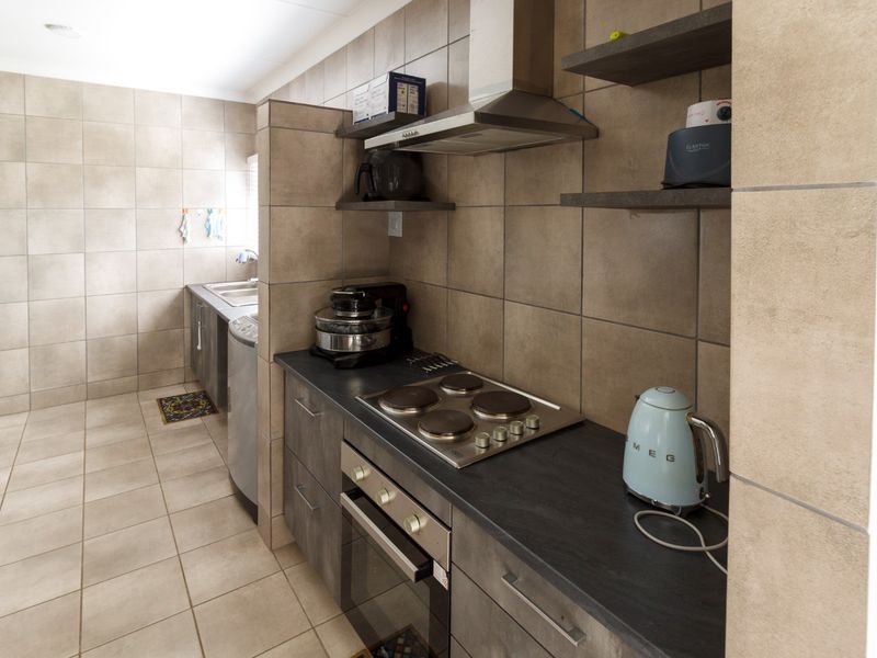A functional kitchen area featuring built-in cabinetry, a stainless steel oven and hob, extractor fan, and tiled flooring throughout.