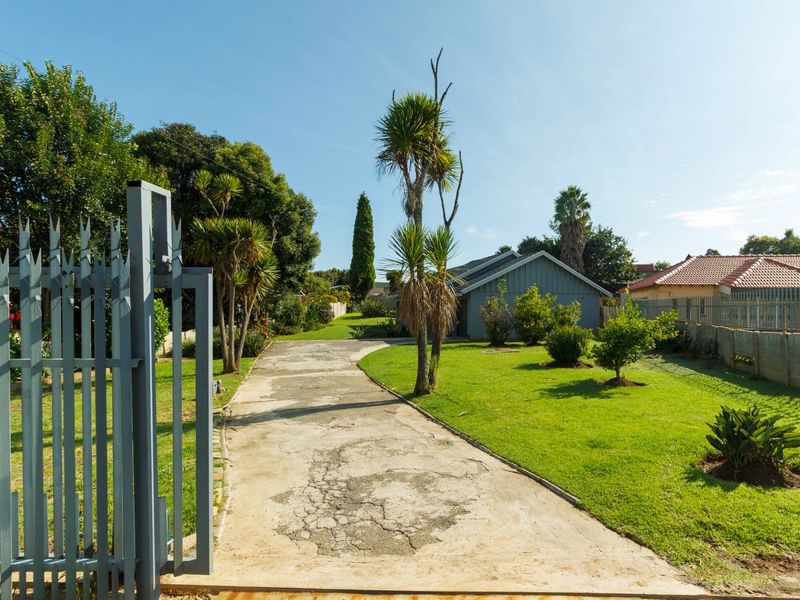 A view of the property entrance featuring a gated driveway, landscaped lawn, and mature trees leading toward the main house structure.