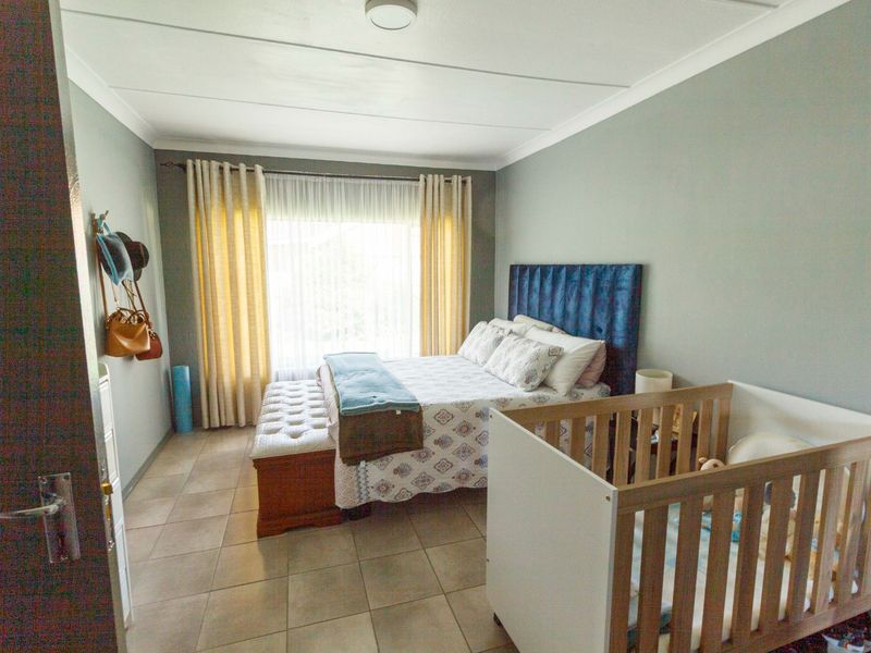 A functional bedroom featuring tiled flooring, neutral wall tones, and large windows with curtain treatments, providing a comfortable and well-lit living space.