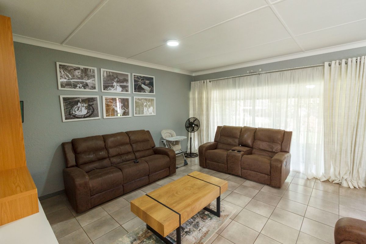 A comfortable living room featuring tiled flooring, neutral wall tones, and large windows with sheer curtains allowing for natural light.