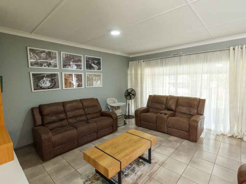 A comfortable living room featuring tiled flooring, neutral wall tones, and large windows with sheer curtains allowing for natural light.