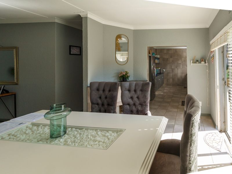 A bright dining area featuring tiled flooring and a seamless transition into the adjacent kitchen space, illuminated by natural light from large windows.