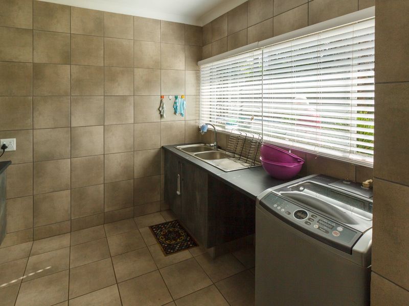 Functional laundry room featuring tiled walls and flooring, a double basin sink, and dedicated plumbing connections for a washing machine.