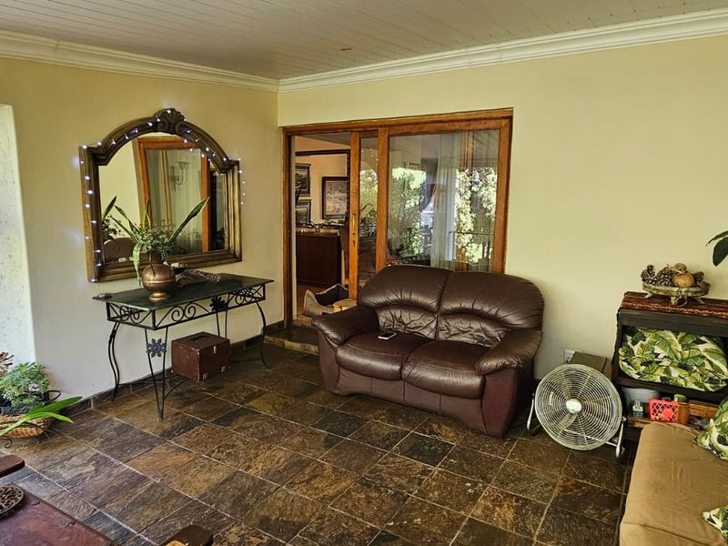 A covered patio area featuring slate tile flooring, timber-framed sliding doors, and large windows providing natural light and garden views.