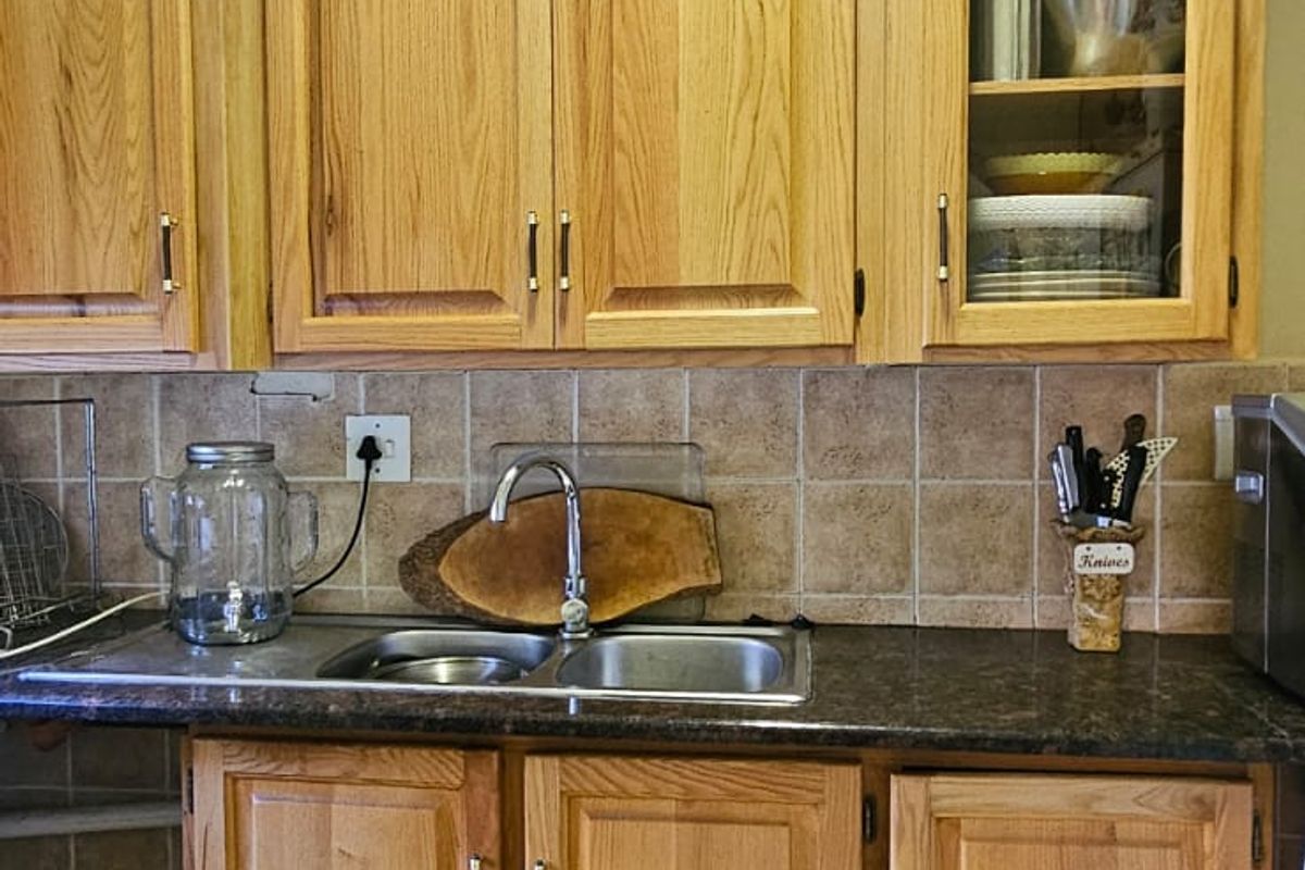 A functional kitchen area featuring traditional oak cabinetry, a double bowl stainless steel sink, and durable ceramic floor tiles.