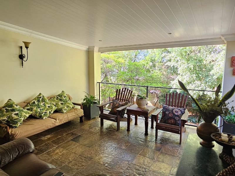 A covered patio area featuring tiled flooring, a tongue and groove ceiling with recessed lighting, and a metal railing overlooking the garden.