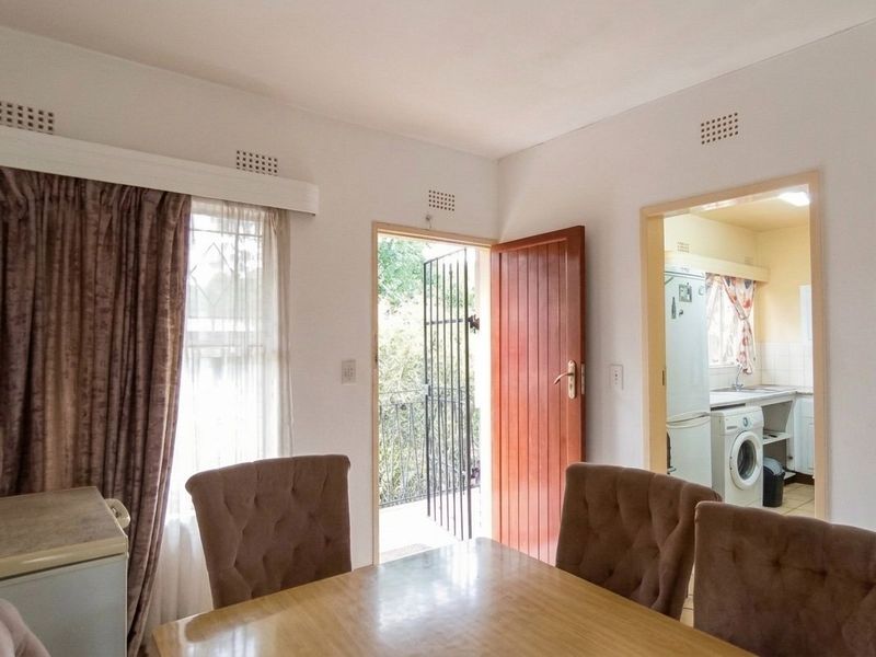 Open plan living area featuring a doorway to a balcony and an adjacent kitchen with built-in cabinetry and laundry plumbing.