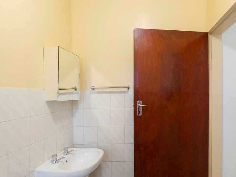 A functional bathroom featuring a wall-mounted basin, tiled splashback, medicine cabinet, and a solid wood door.