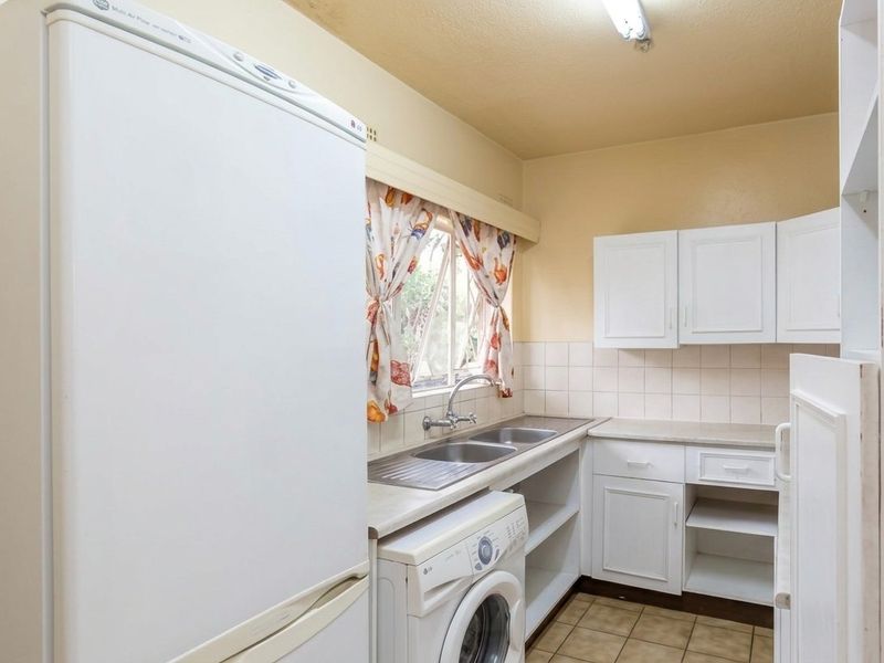 A functional kitchen featuring white cabinetry, double basin sink, tiled splashback, and tiled flooring, offering a practical layout for daily use.