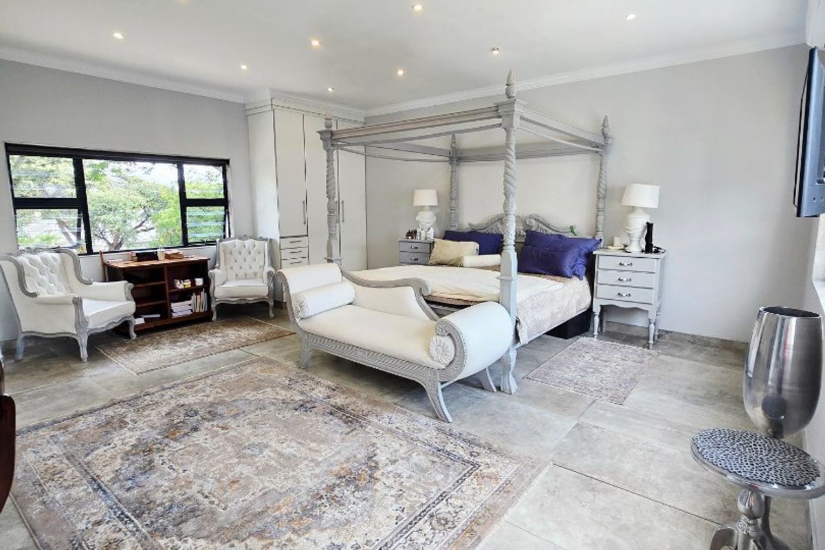 Spacious bedroom featuring large format floor tiles, recessed downlighting, built-in cabinetry, and large aluminium-framed windows providing natural light.
