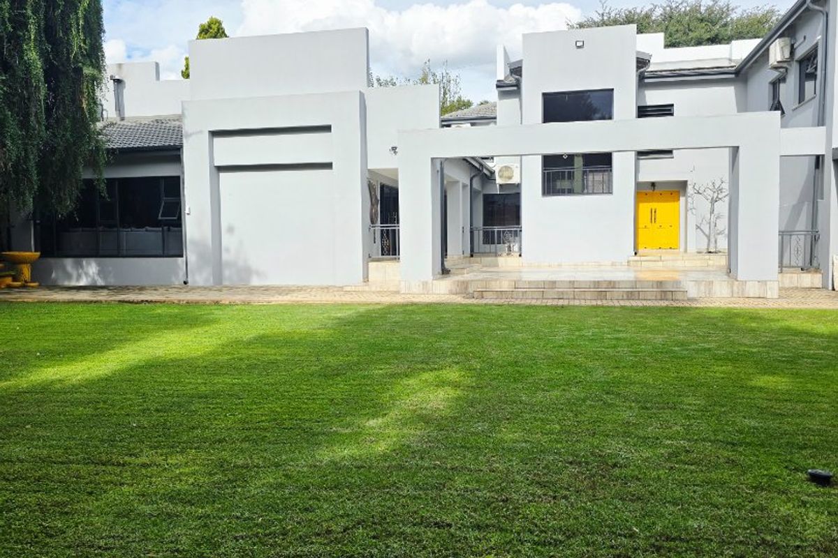 A spacious rear garden featuring a well-maintained lawn and a modern architectural facade with a paved patio area.