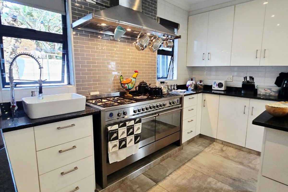 Modern kitchen featuring a large gas range, stainless steel extractor fan, farmhouse sink, granite countertops, and white cabinetry with subway tile backsplash.