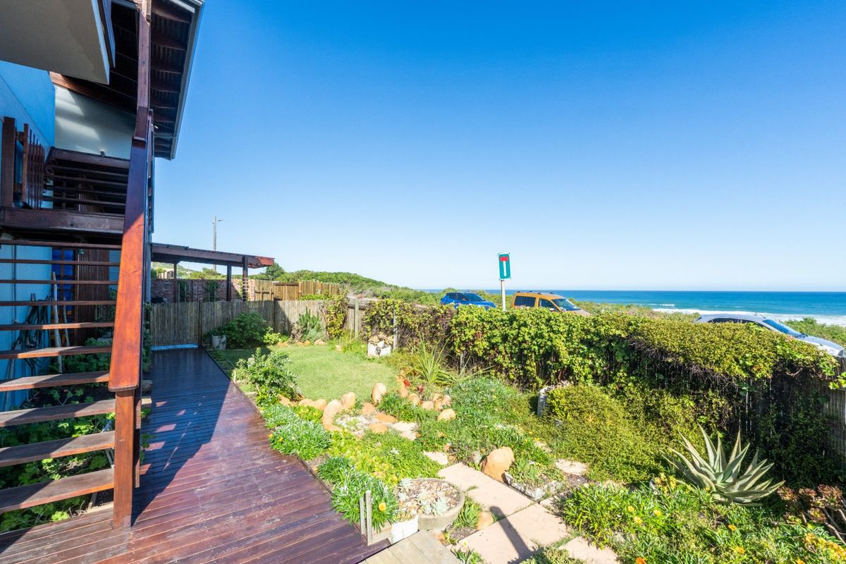 Rear exterior view featuring a timber deck, staircase, and landscaped garden with ocean views in the background.