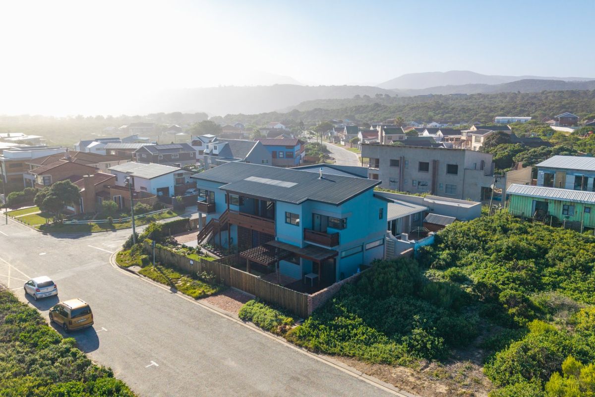 Aerial view of a blue two-story residential property featuring a metal roof, solar panels, and timber decking, situated in a coastal neighborhood.