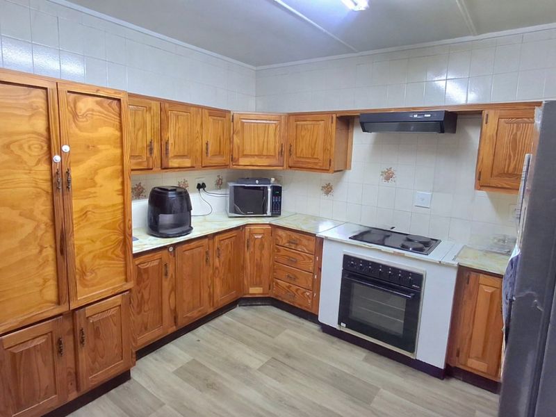 A functional kitchen featuring traditional wooden cabinetry, laminate countertops, a built-in oven with electric hob, and a tiled splashback.