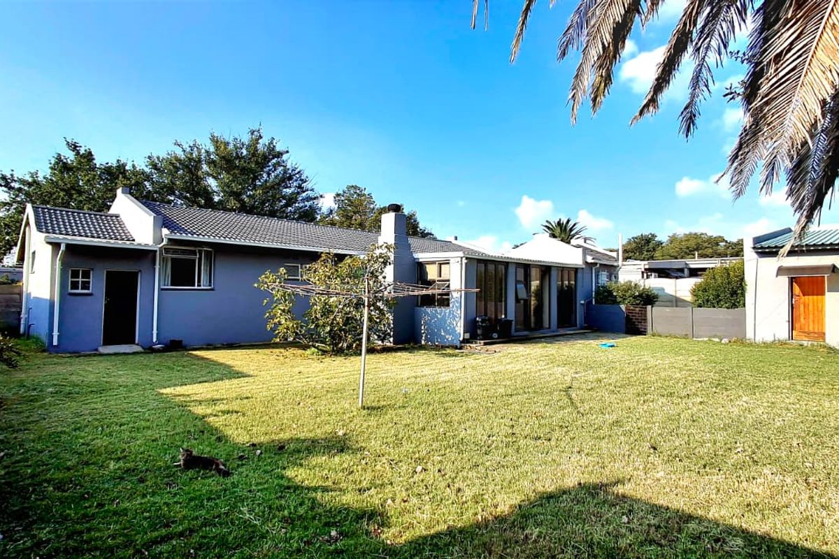 Rear view of the house featuring a spacious lawn, tiled roof, chimney, and sliding glass doors leading to the backyard.
